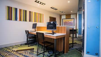 A modern office space with a desk, chairs, and a computer. There is a colorful abstract painting on the wall and a patterned carpet.