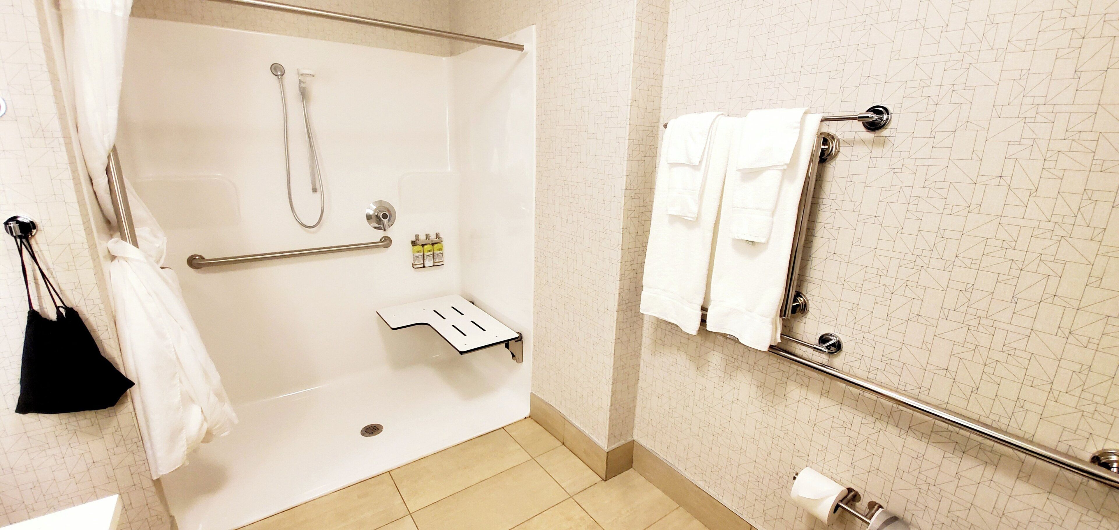 A shower area with a glass door, a towel rack with towels, and a handrail.