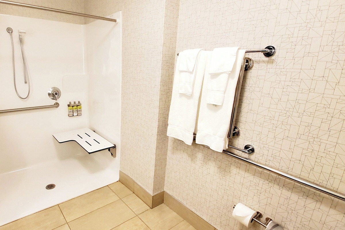 A shower area with a glass door, a towel rack with towels, and a handrail.