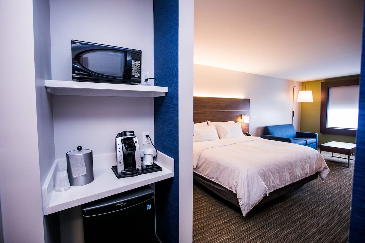 A hotel room with a bed, a desk with a microwave, coffee maker, and a trash bin.