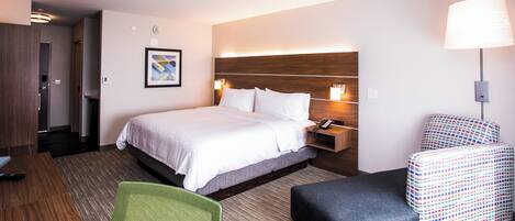 Una habitación de hotel con cama, mesita de noche, lámpara, silla y un cuadro en la pared.