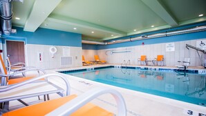 An indoor swimming pool with orange chairs, a diving board, and pool rules signs.
