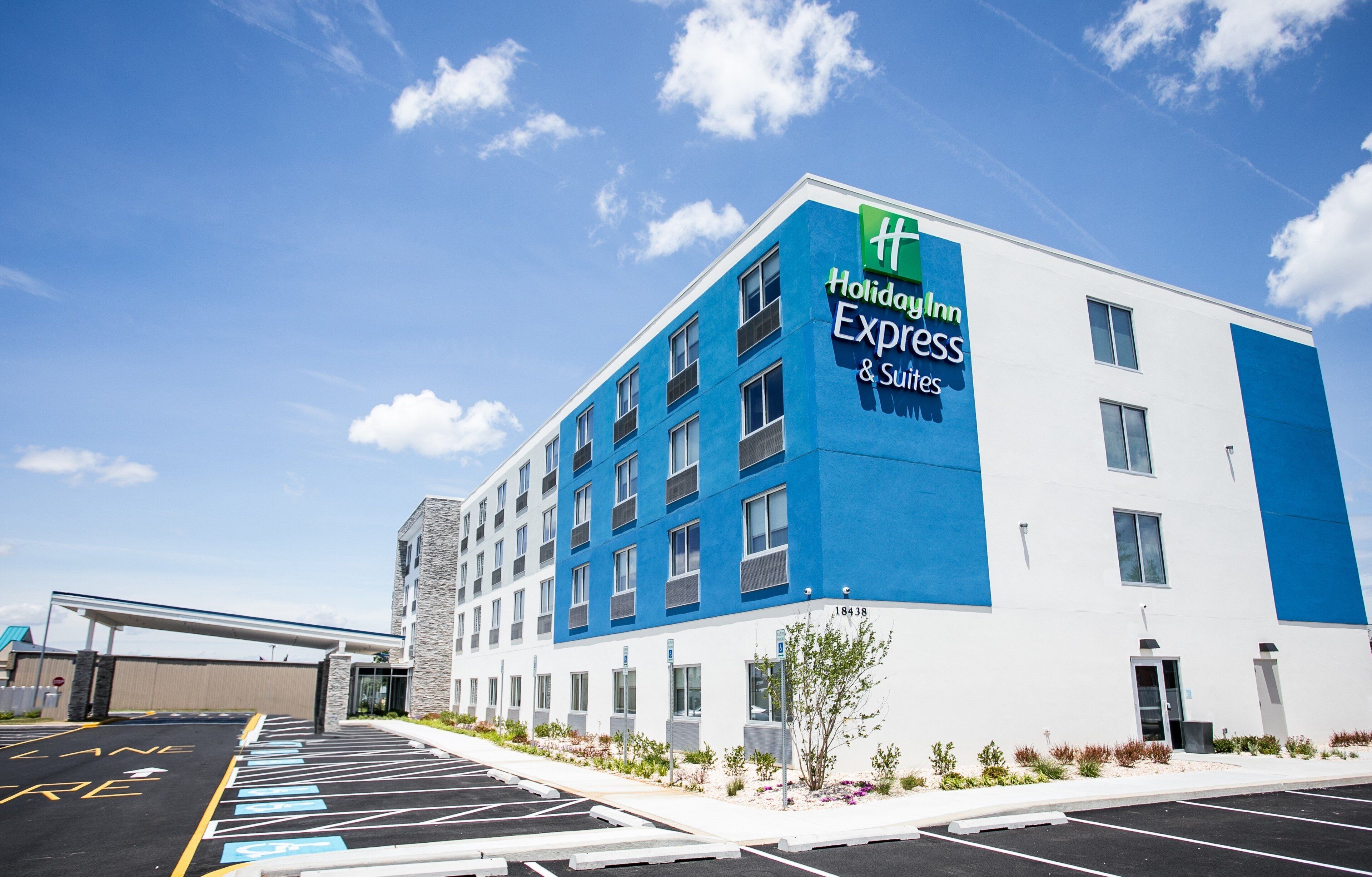 Ein Holiday Inn Express & Suites Gebäude mit blau-weißer Fassade, Parkplatz und blauem Himmel.