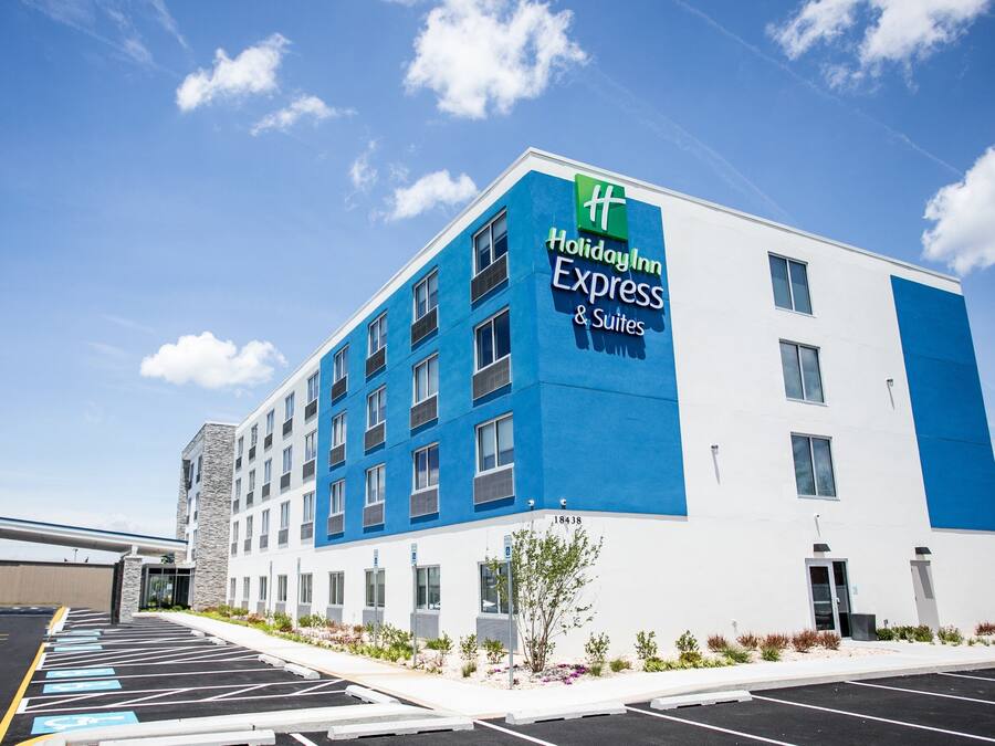 A Holiday Inn Express & Suites building with a blue and white facade, parking lot, and a clear sky.
