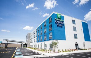 A Holiday Inn Express & Suites building with a blue and white facade, parking lot, and a clear sky.