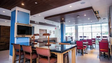A modern restaurant interior with a bar area, seating, and a large window providing natural light.