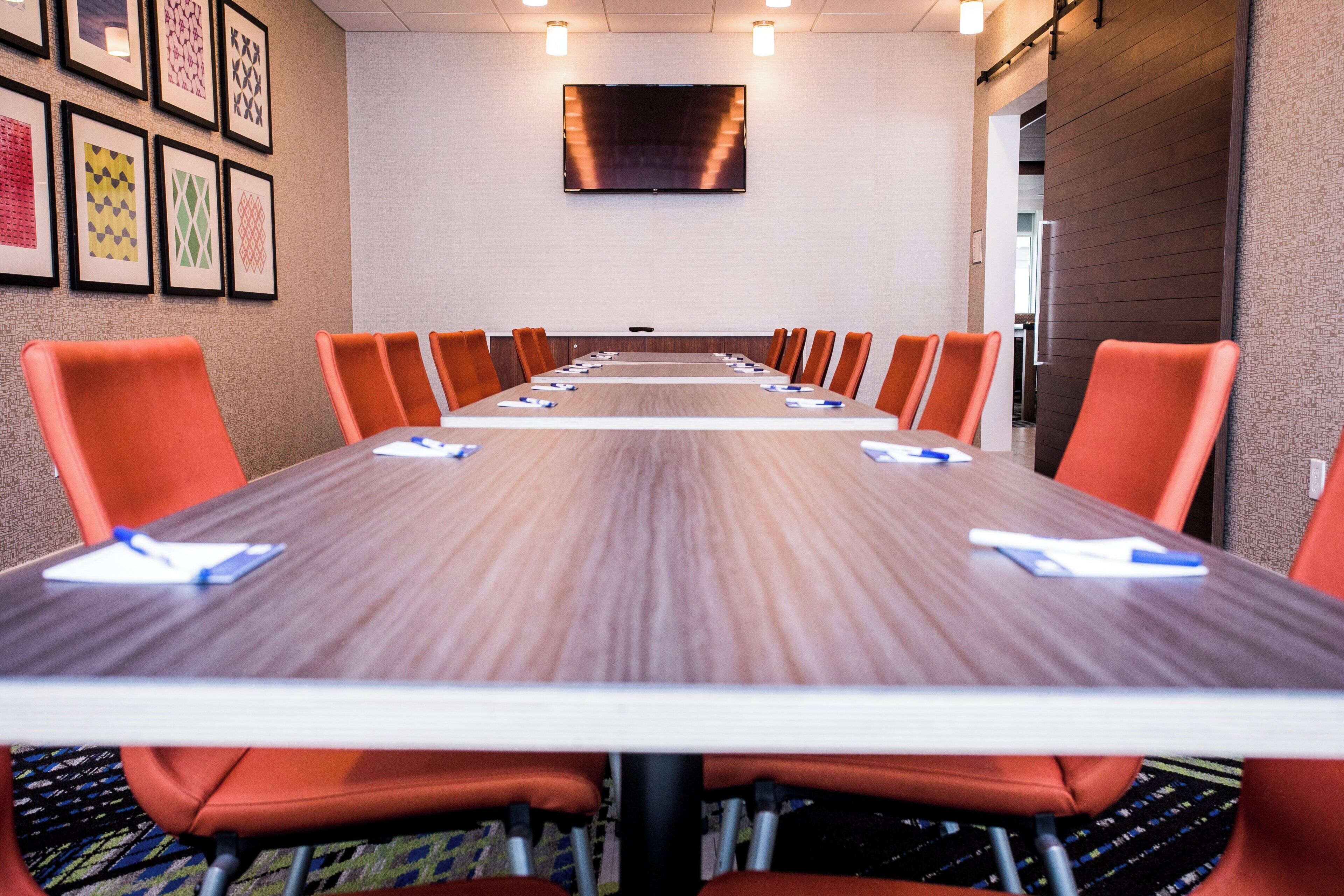 A conference room with a long table, orange chairs, and framed artwork on the walls.