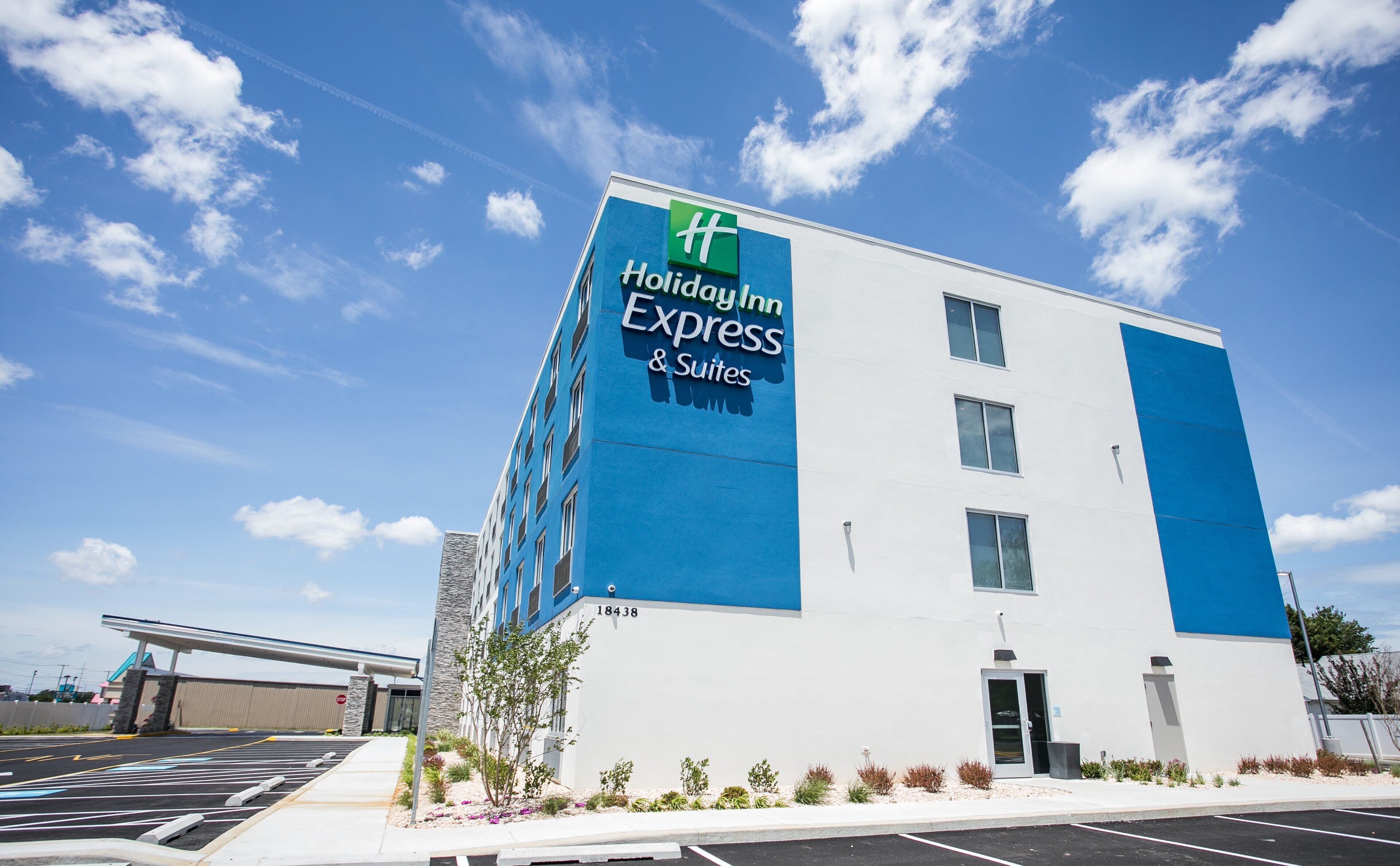 A Holiday Inn Express & Suites building with a blue and white facade, a parking lot, and a clear sky.