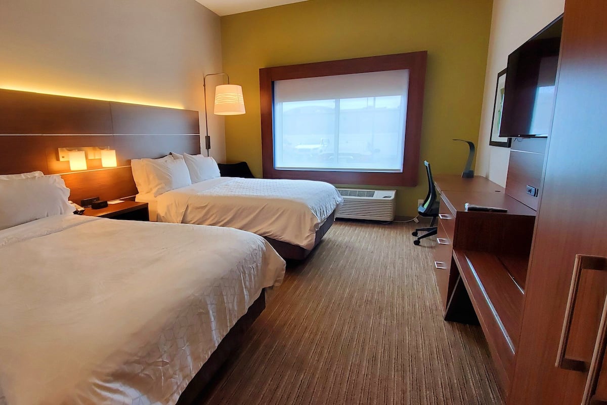 A hotel room with two beds, a desk, a TV, and a window with blinds.