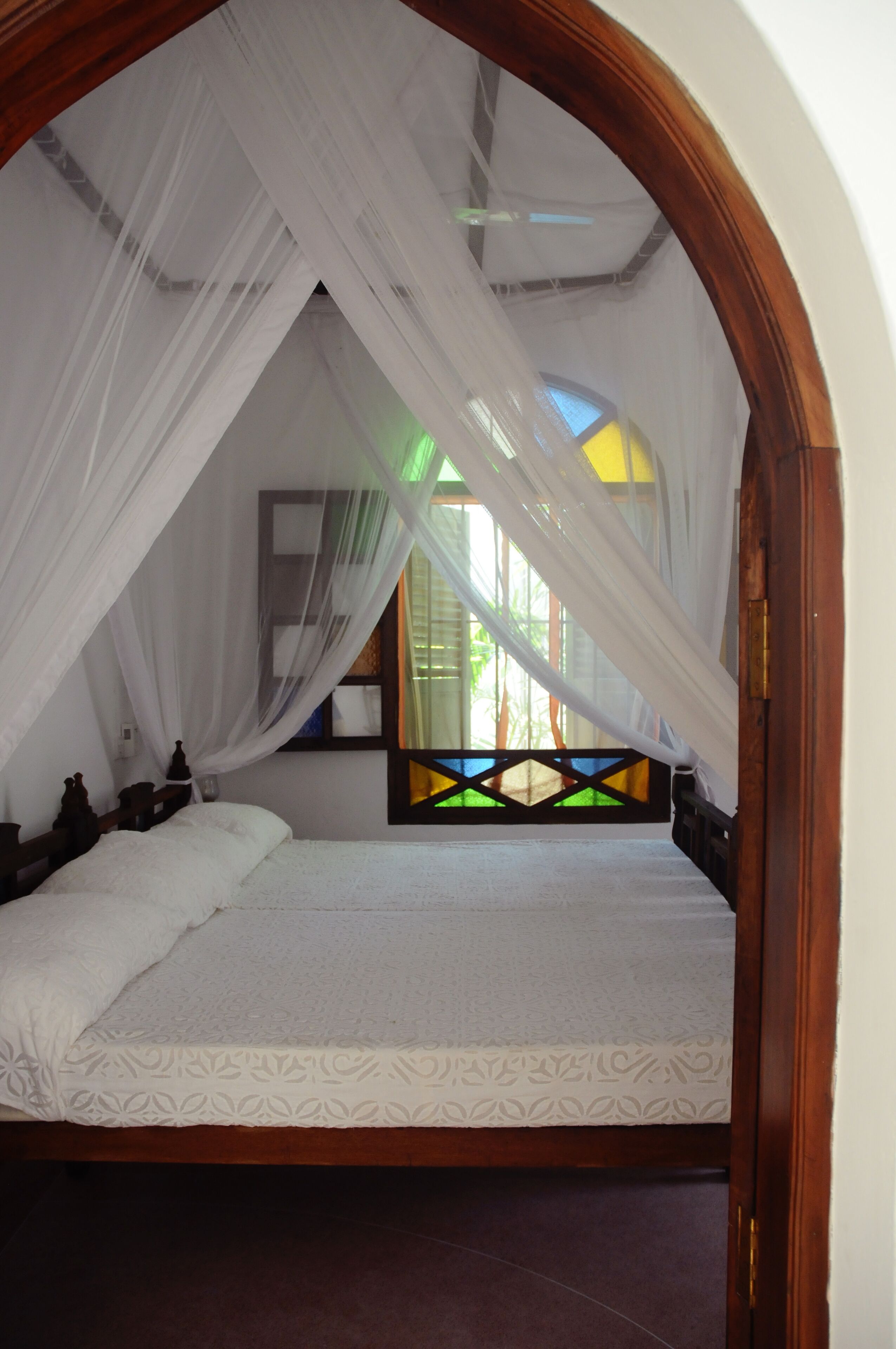 A room with a bed under a white canopy, a wooden door frame, and a window with a green and yellow view.