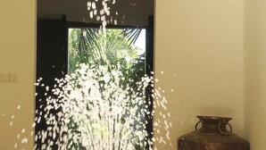 Uma fonte com jatos de água em um espaço com chão de azulejos e um vaso sobre uma mesa.
