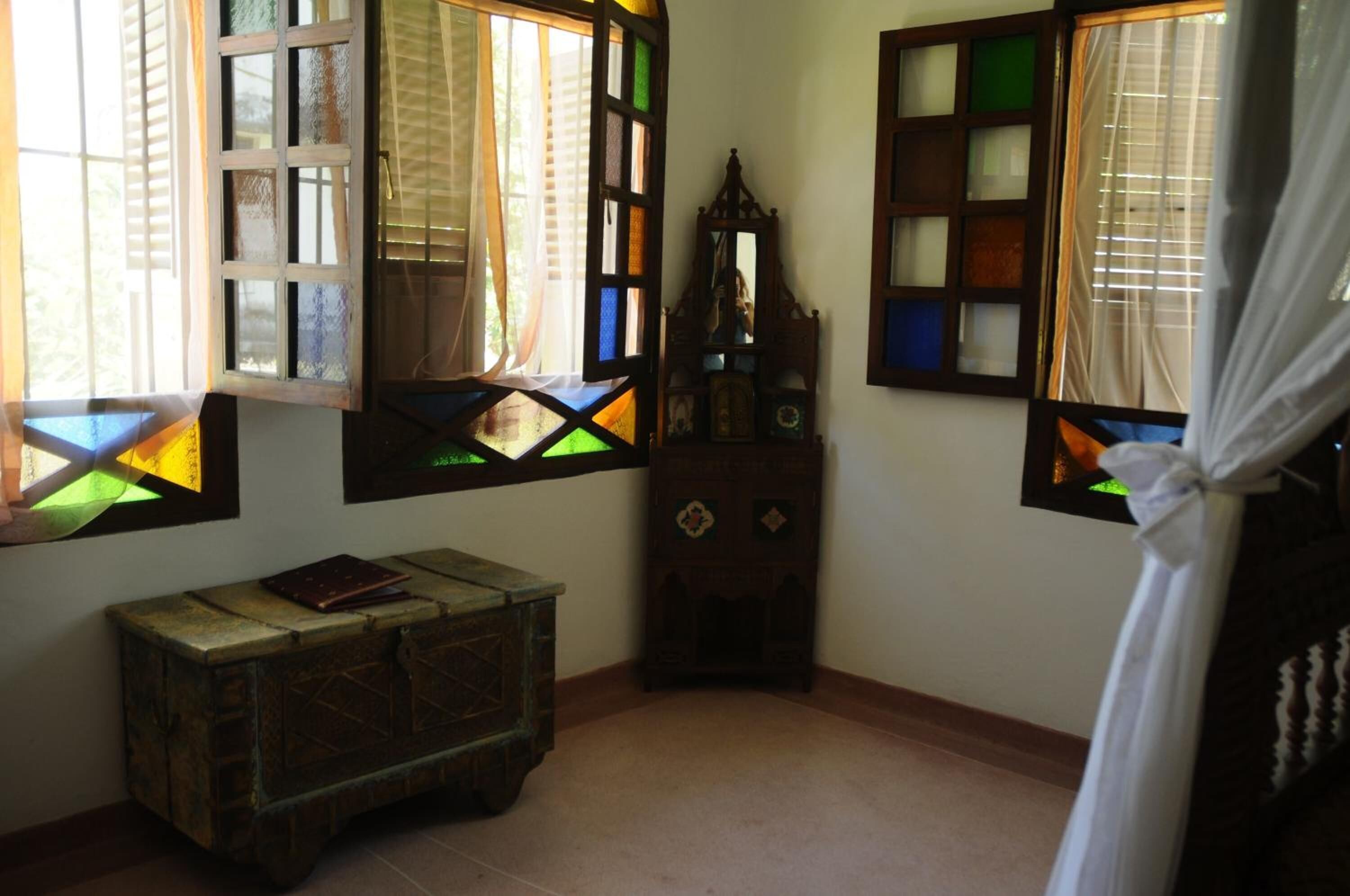 A room with a wooden chest, a mirror, and stained glass windows.