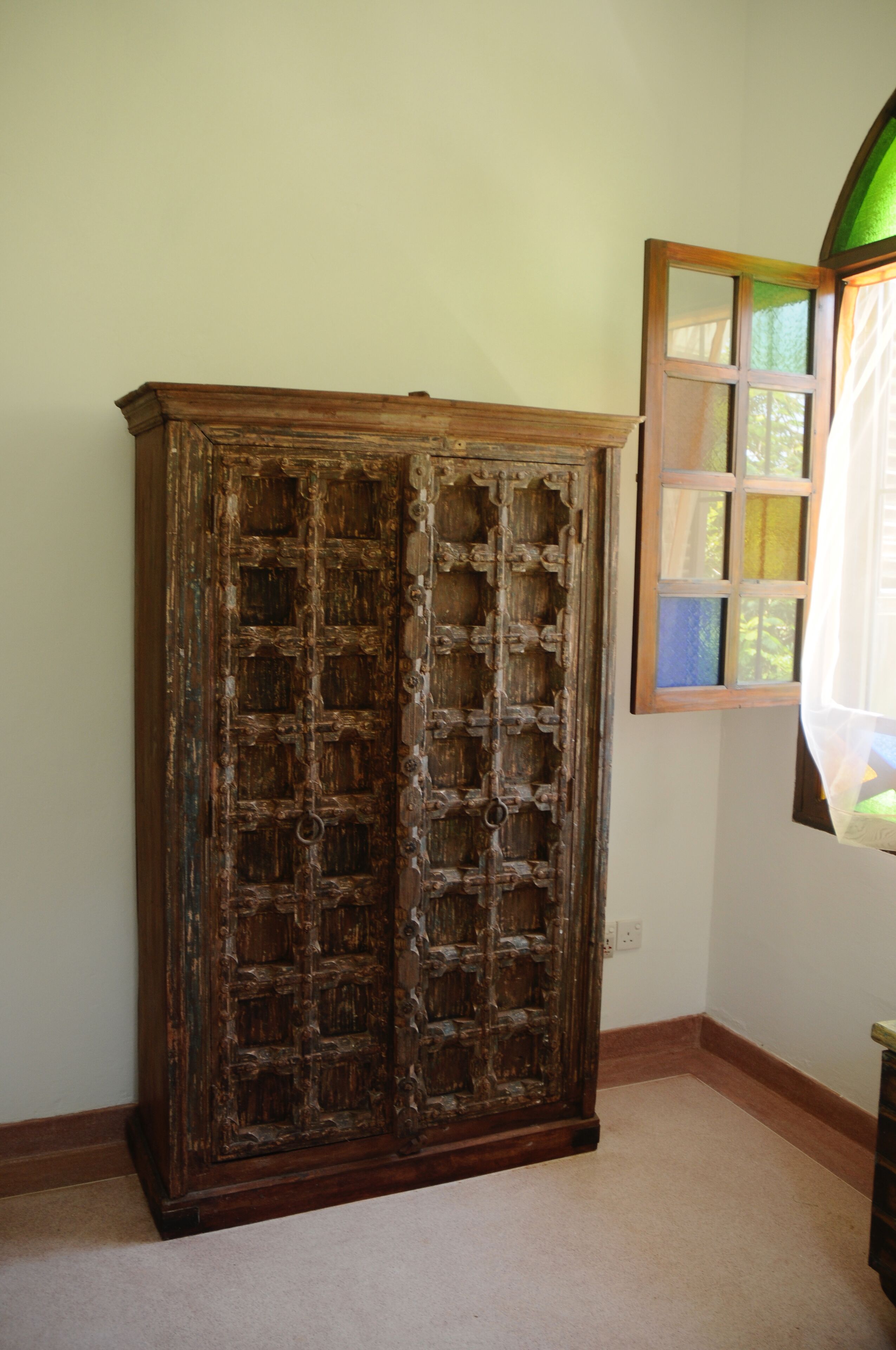 A wooden cabinet with multiple compartments, a window with stained glass, and a carpeted floor.