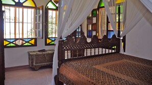 Quarto com cama de madeira, mesa de cabeceira e janela com vitrais.