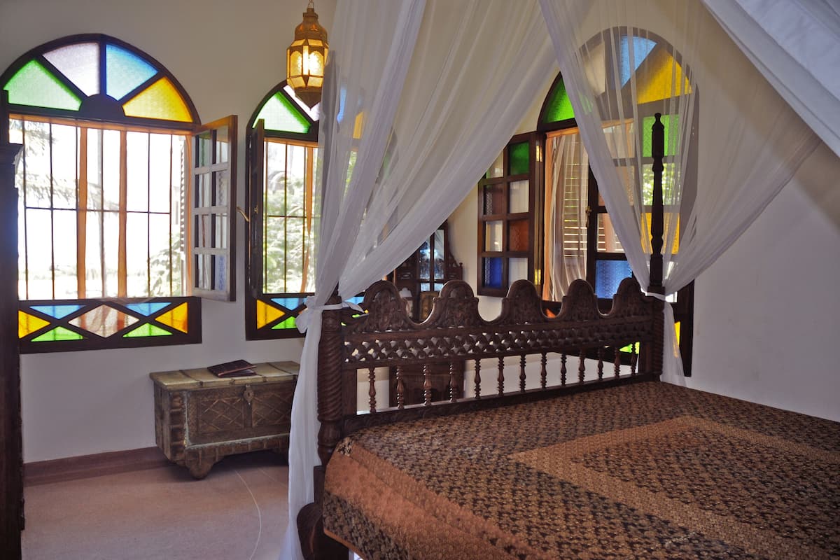 A bedroom with a wooden bed, a nightstand, and a window with stained glass.