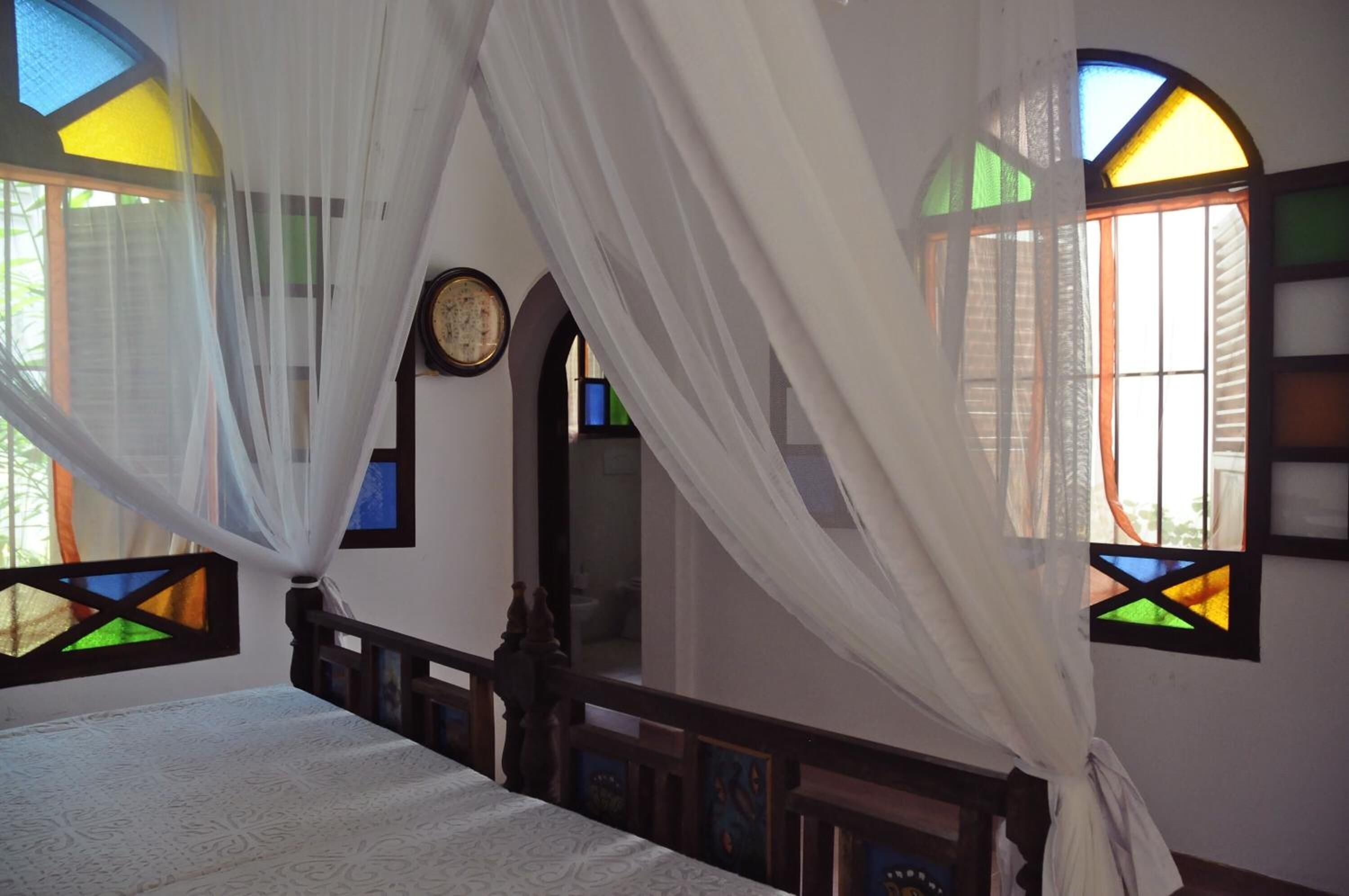 A room with a bed, a clock on the wall, and stained glass windows.