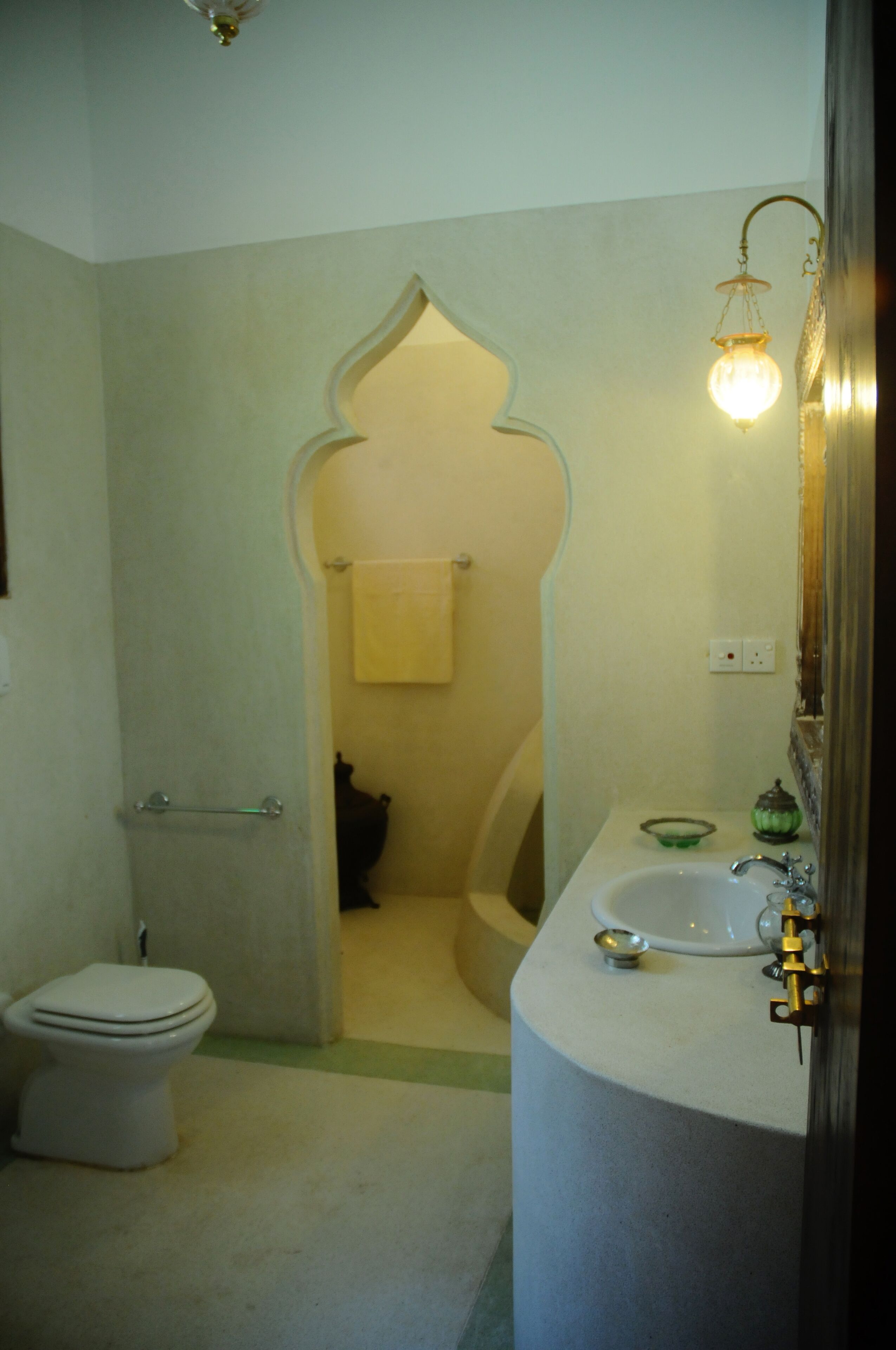 Un baño con inodoro, lavabo y espejo. Hay una toalla colgada en la pared y una lámpara sobre el espejo.