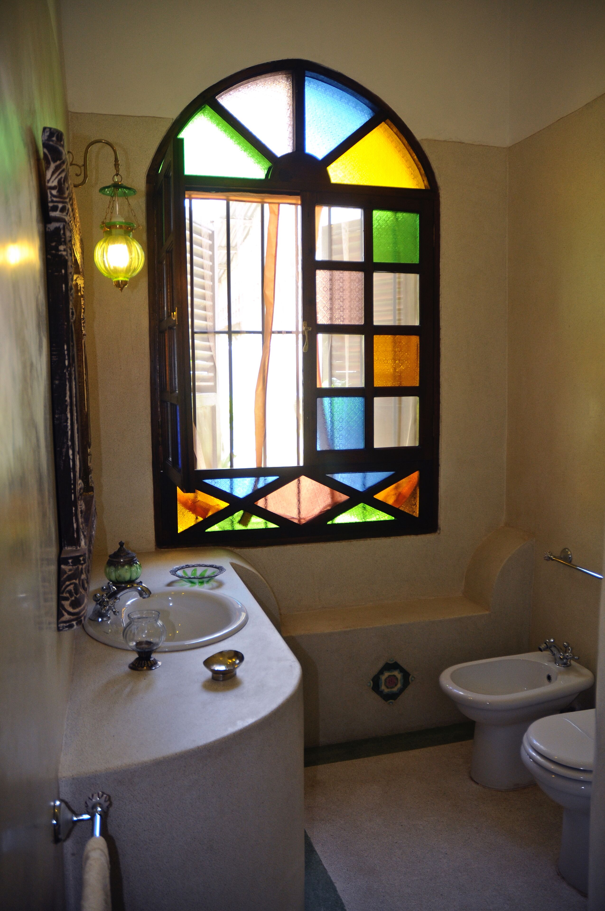 A bathroom with a curved sink, a bidet, and a stained glass window.