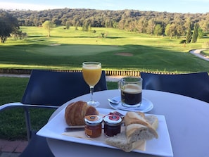 Een tafel met croissants, jam en koffie, met uitzicht op een golfbaan.