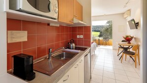 A modern kitchen with a built-in microwave, a kettle, and a coffee maker. There is a dining area with a table and chairs visible through an open door. - Golf & Résidence de Nîmes Vacquerolles (Nîmes)