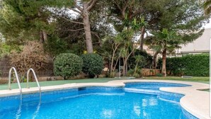 A swimming pool with a tiled edge, surrounded by various trees and shrubs. - Ronda Playa, apartment with pool just a step away from the sea. (Can Picafort)
