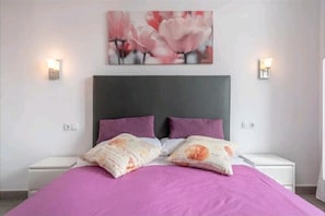 A bedroom with a bed, two nightstands, a headboard, and a wall-mounted light fixture.