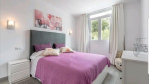 A bedroom with a bed, nightstands, a desk, a window with curtains, and a wall-mounted light fixture. - Ronda Playa, apartment with pool just a step away from the sea. (Can Picafort)