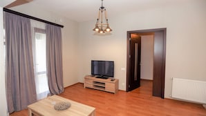 A room with a wooden floor, a television on a wooden stand, a table with a decorative bowl, and a door leading to another room. - One Bedroom apartment for shopaholics (Tbilisi)