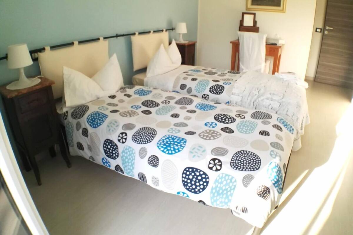 A double bed with a patterned bedspread, two bedside tables with lamps, a nightstand, and a framed picture on the wall.