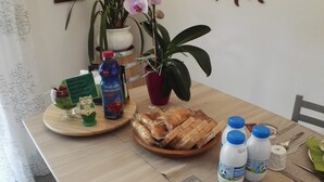 A dining table with a plate of bread, a bottle of juice, and a cup. There are chairs around the table and a potted plant. - B&B Guglielmina (Quarna Sotto)