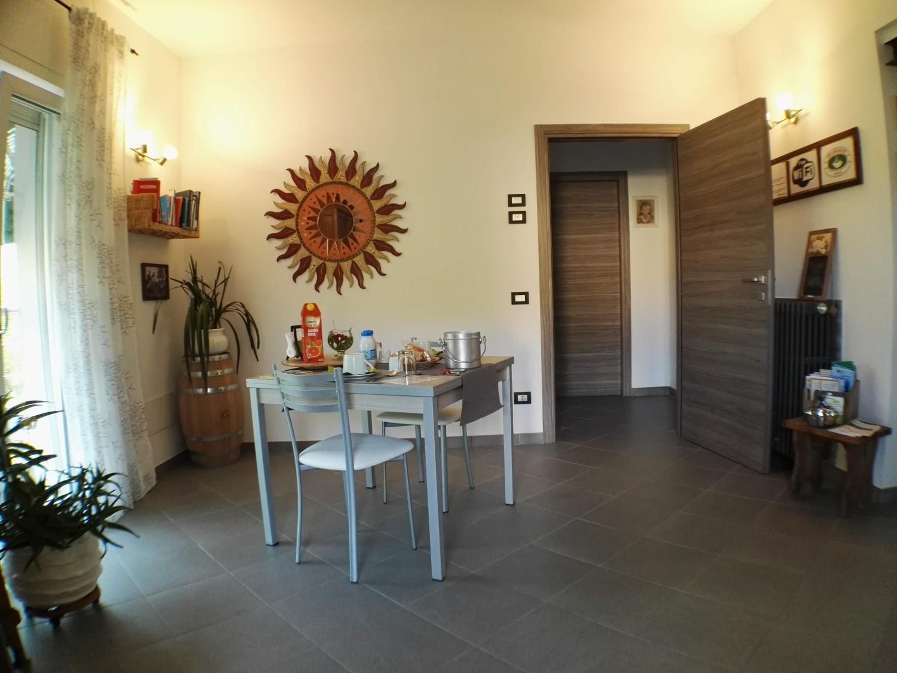 Ein Essbereich mit einem für zwei Personen gedeckten Tisch, Wandkunst in Sonnenstrahlform und einer Holztür im Hintergrund.