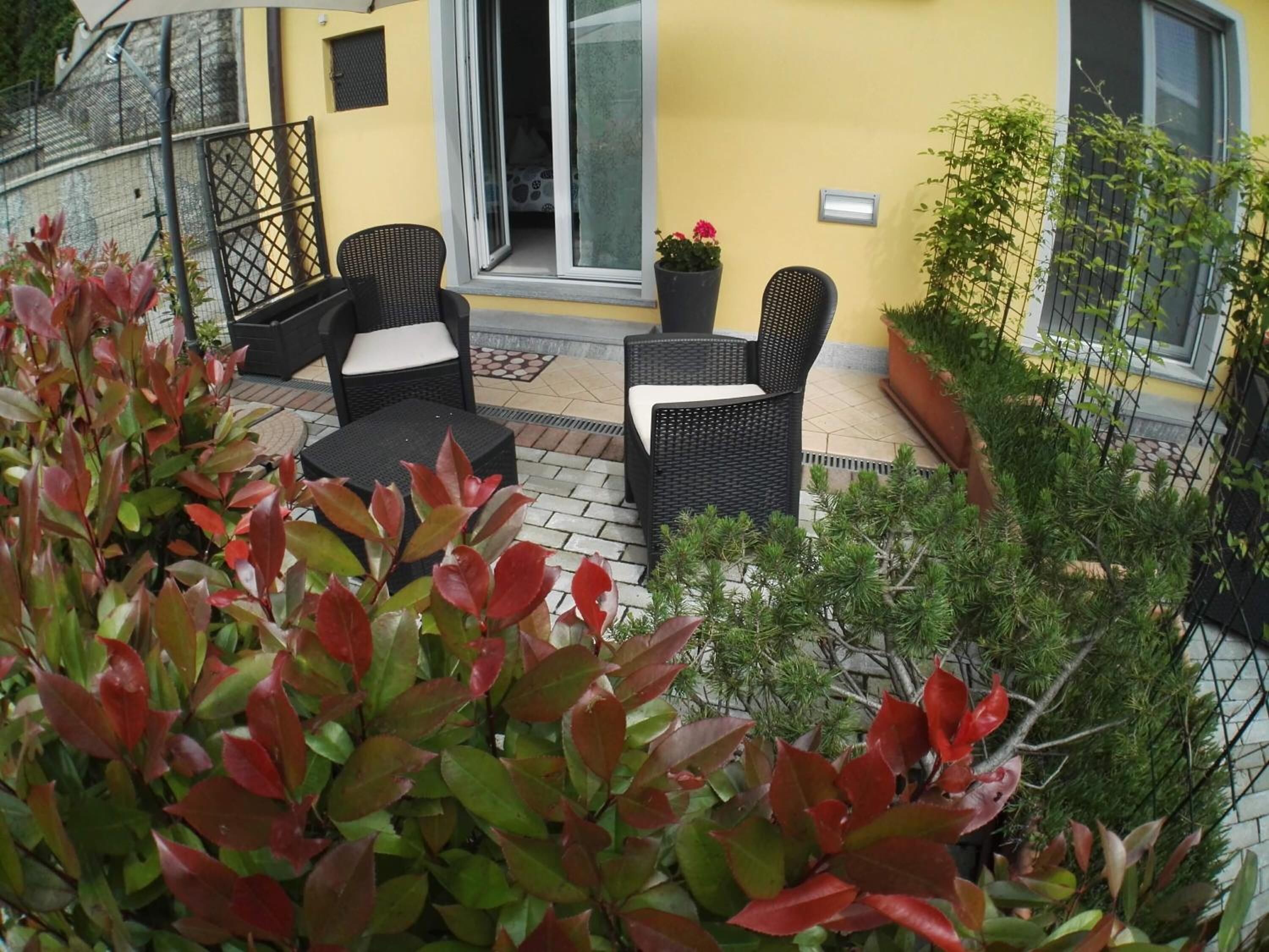 An outdoor patio area with wicker furniture, potted plants, and a yellow wall.