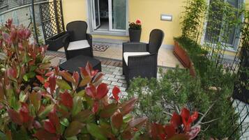 An outdoor patio area with wicker furniture, potted plants, and a yellow wall.