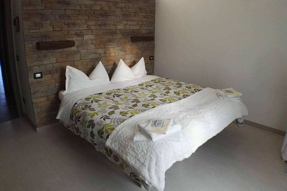 A neatly made bed with a floral bedspread and white pillows, positioned against a brick wall with a wooden headboard.