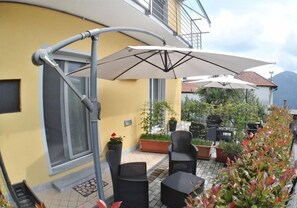 An outdoor patio area with wicker furniture, a large umbrella, and potted plants. - B&B Guglielmina (Quarna Sotto)