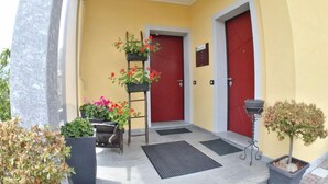 A hotel entrance with two red doors, a small outdoor seating area, and potted plants. - B&B Guglielmina (Quarna Sotto)