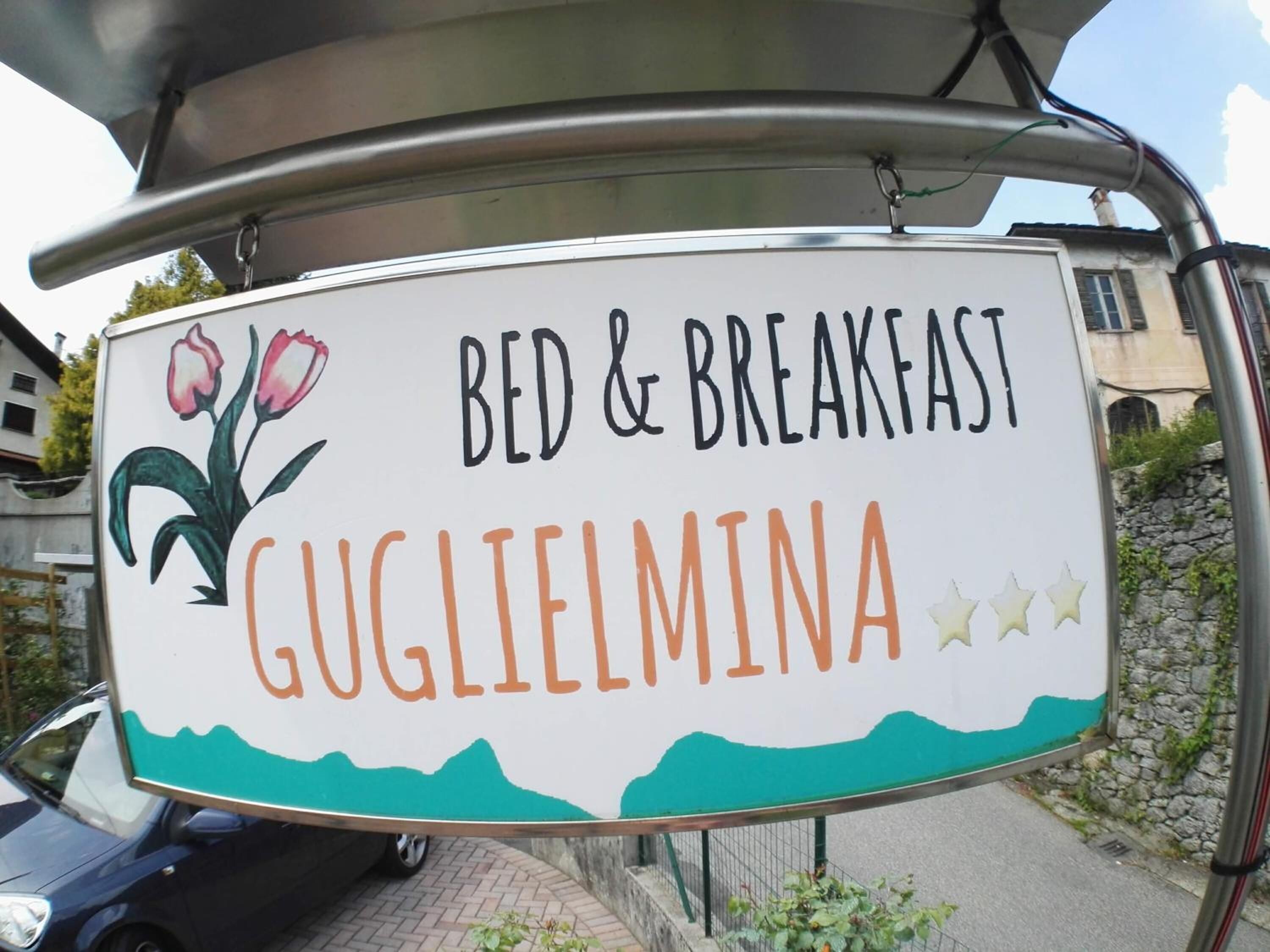 Segnaletica per un bed and breakfast chiamato Guglielmina, con un’illustrazione di tulipani e un paesaggio montano.