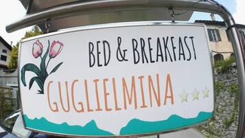 Segnaletica per un bed and breakfast chiamato Guglielmina, con un’illustrazione di tulipani e un paesaggio montano.