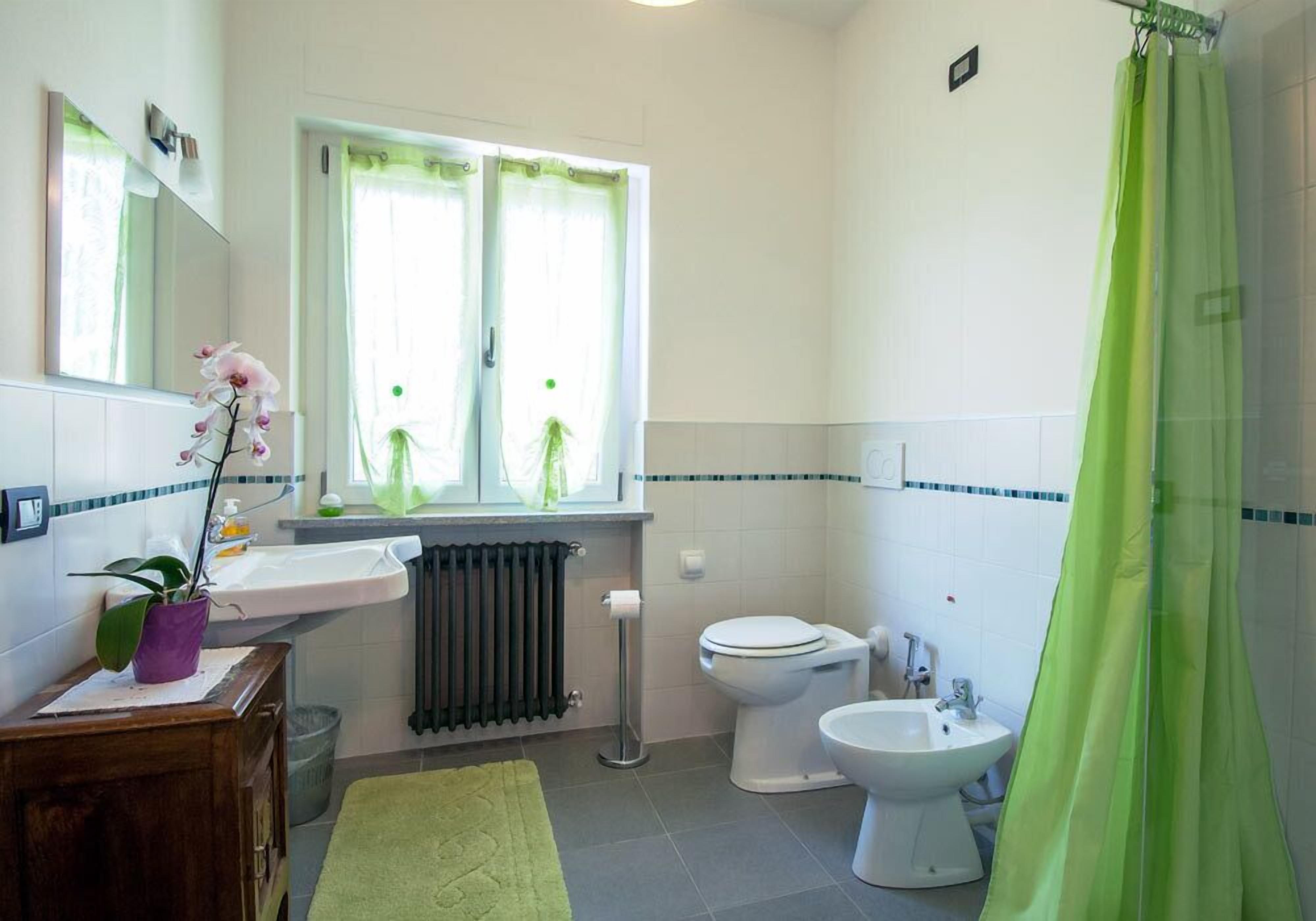 A bathroom with a toilet, bidet, sink, and a green shower curtain.