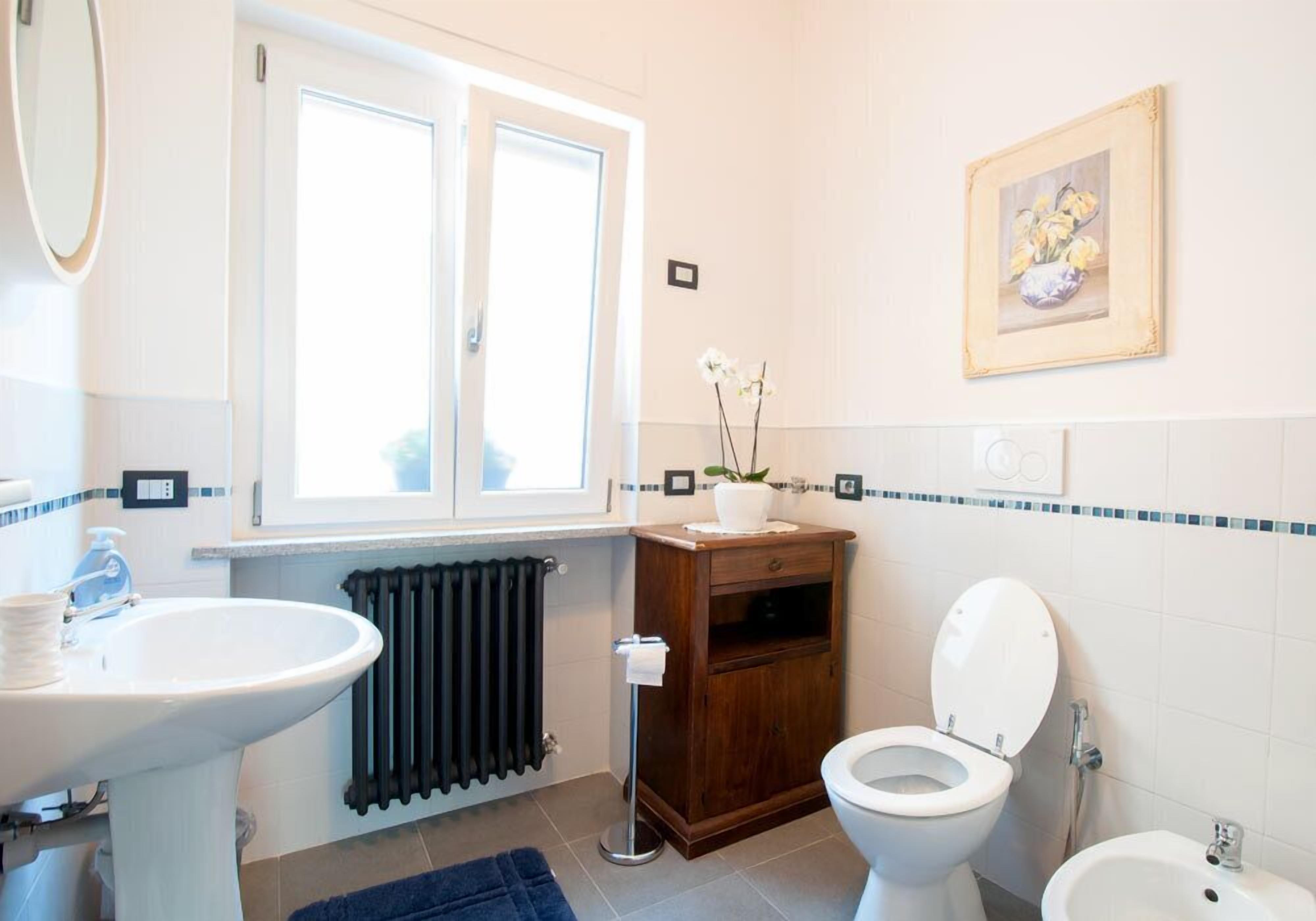 A bathroom with a sink, toilet, bidet, and a window with blinds.