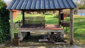 A rustic outdoor barbecue area with a metal roof, a brick table, and a metal grill.