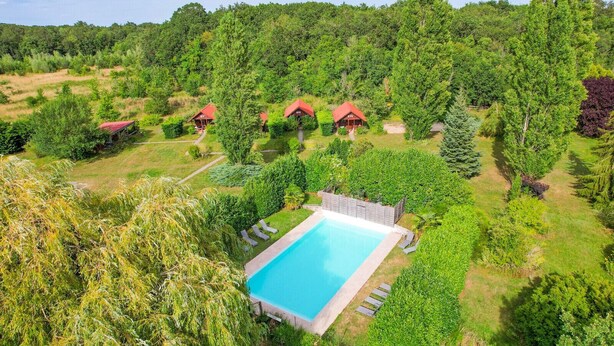 A resort with a swimming pool, several red-roofed cabins, and lush greenery.
