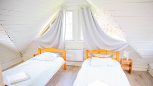 A small attic bedroom with two wooden beds, a window with curtains, and a radiator.