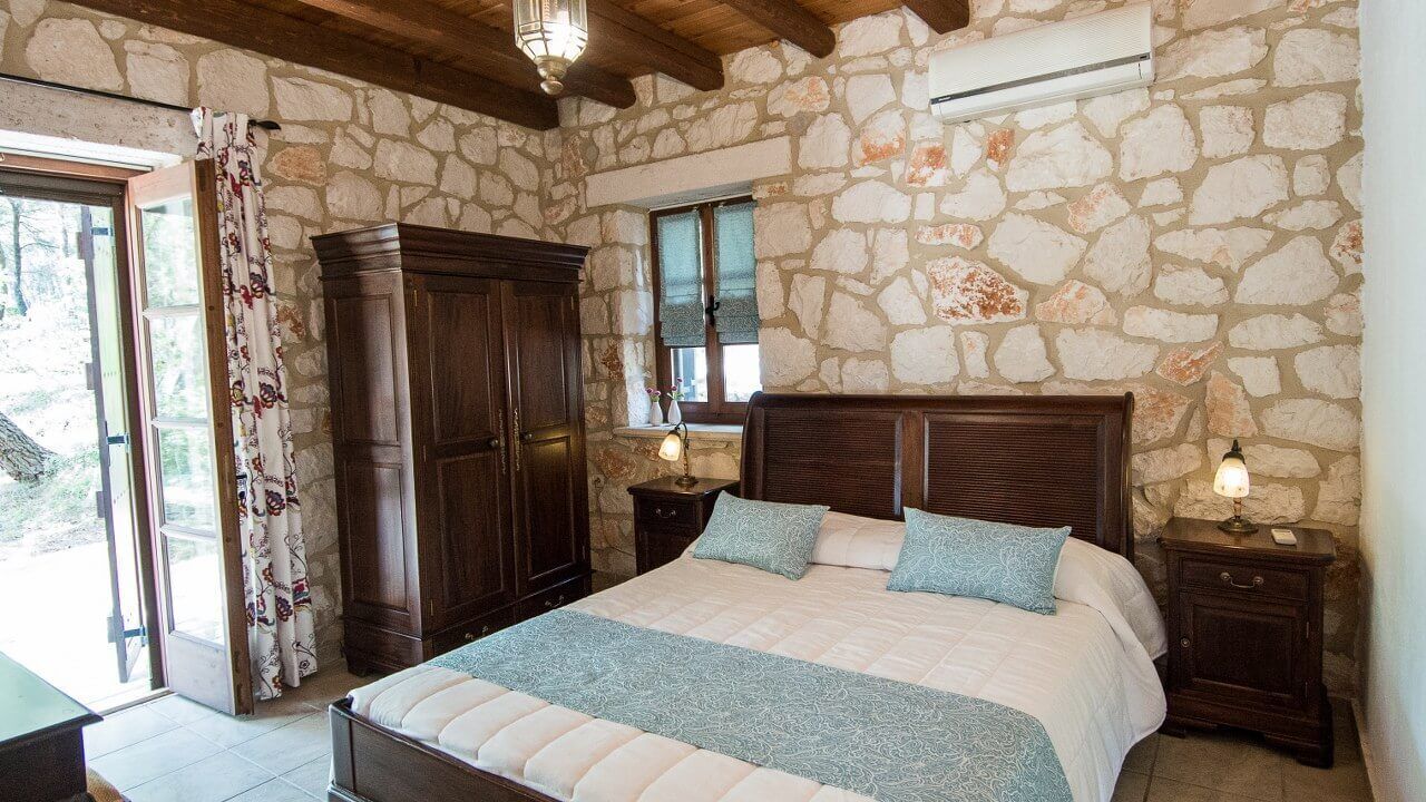Une chambre avec un mur en pierre, un cadre de lit en bois et une table de chevet avec une lampe.