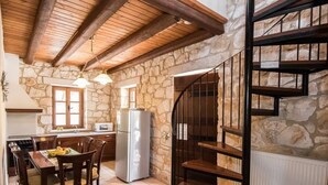 A rustic kitchen with stone walls, wooden beams, a refrigerator, and a dining area with chairs and a table. - Boschetto Holiday Village (Zakynthos)