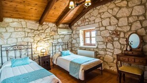 A rustic bedroom with two beds, stone walls, wooden beams, a window, a mirror, and a dresser. - Boschetto Holiday Village (Zakynthos)