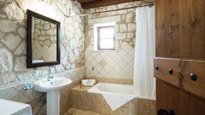 A bathroom with a stone wall, a white sink, a bathtub, and a wooden door.