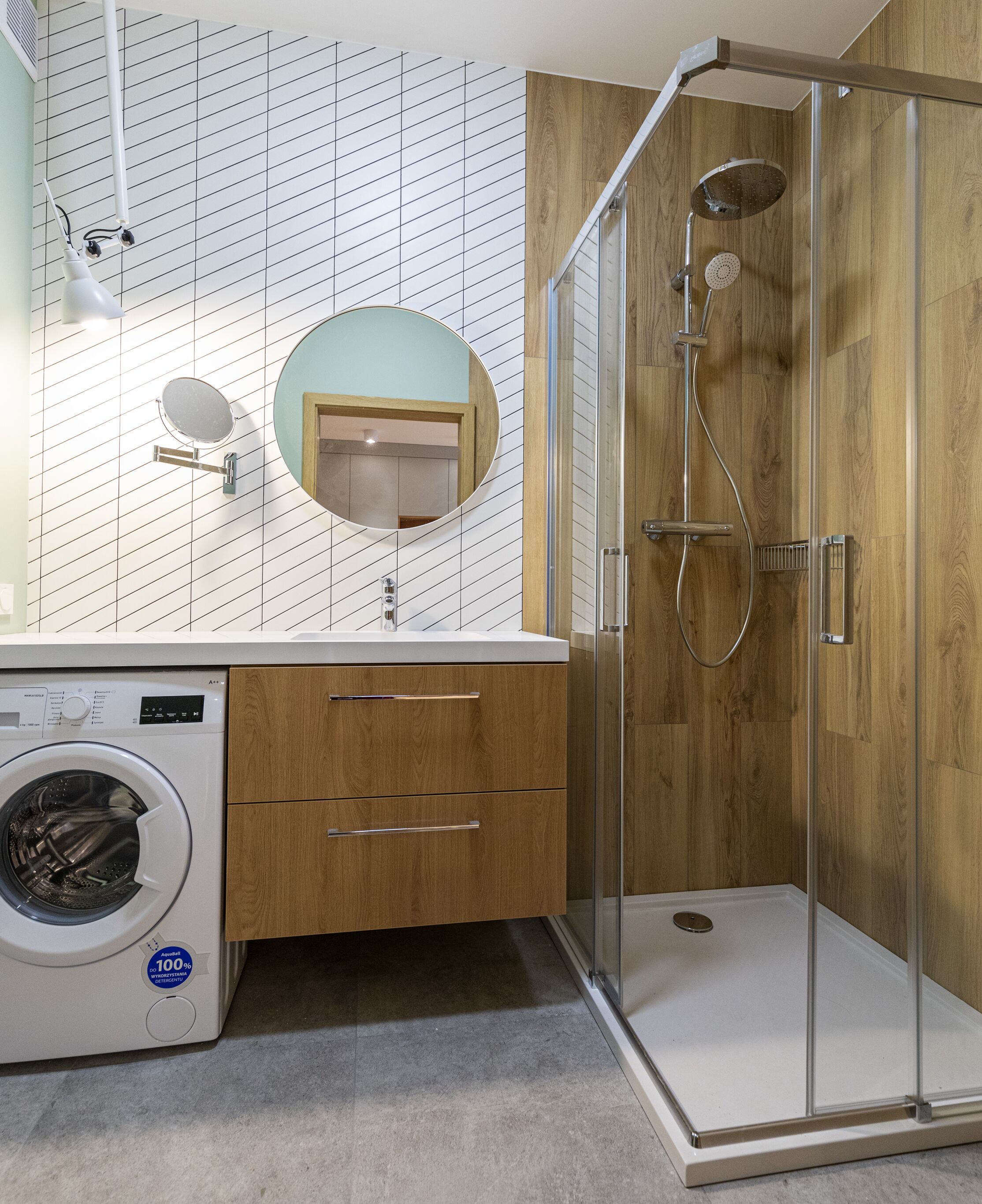 Une salle de bain moderne avec une douche à parois de verre, un lave-linge encastré et un meuble-lavabo en bois.
