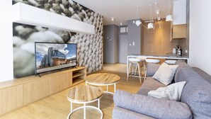 Un salon moderne doté d’un téléviseur à écran plat, d’un canapé gris, d’une table basse en bois et d’un coin cuisine avec un bar.