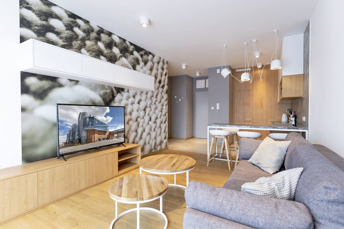 Un salón moderno con un televisor de pantalla plana, sofá gris, mesa de centro de madera y una zona de cocina con barra.